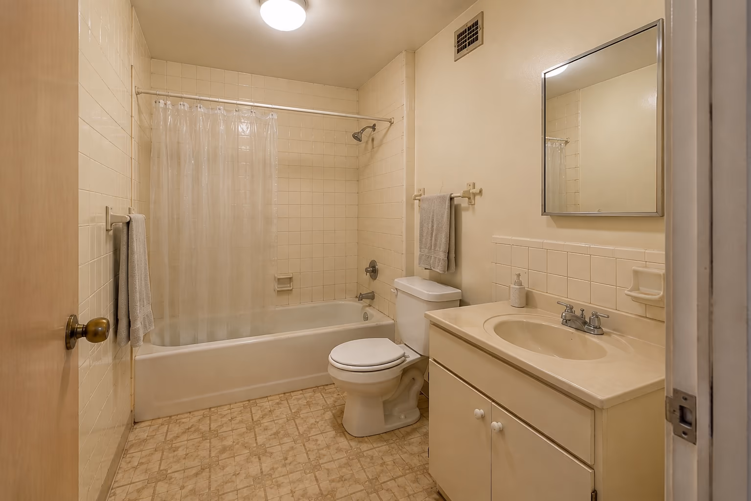 Dated bathroom before an AI redesign, with cream wall tiles, a bath behind a plastic shower curtain and a boxy vanity