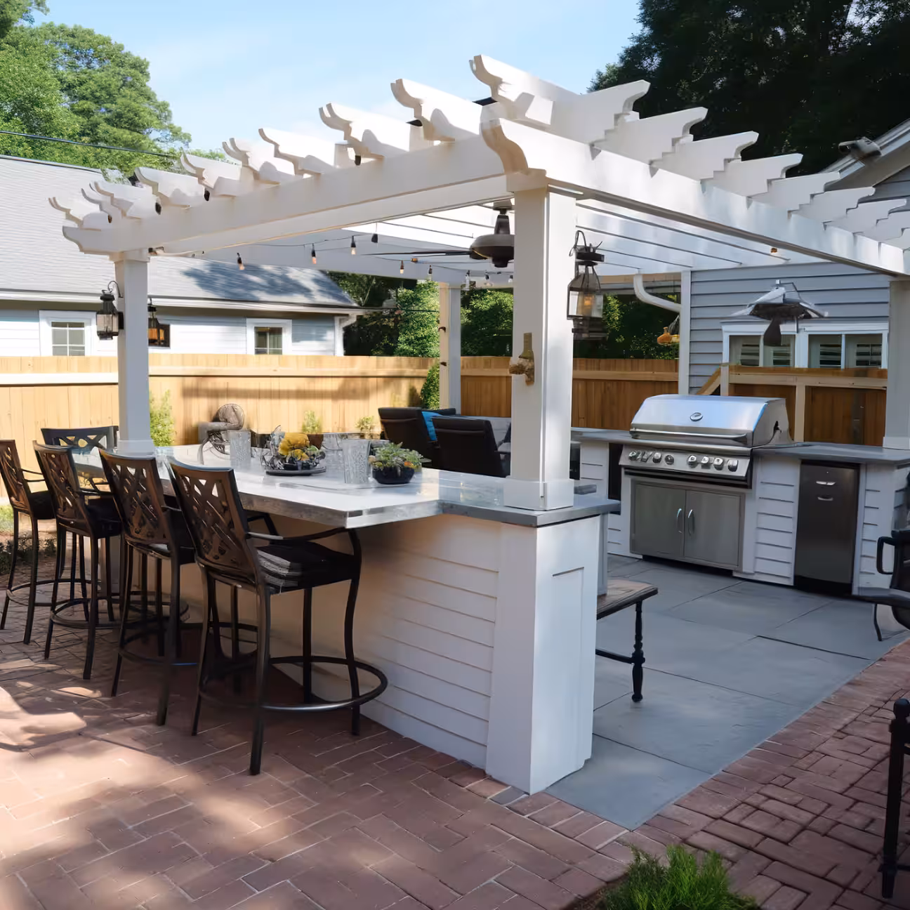 Modern outdoor kitchen with a built in grill stone countertops and bar seating under a patio surrounded by greenery.