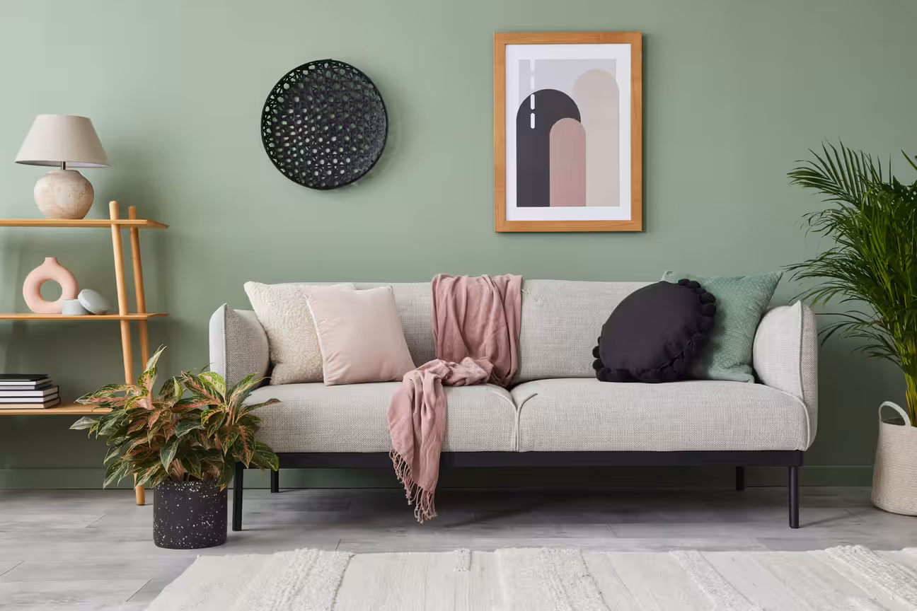 Modern living room with green accent wall, neutral sofa, decorative cushions, indoor plants, and minimal wall art