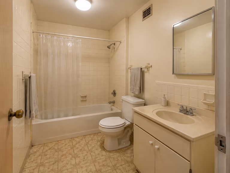 Dated bathroom before an AI redesign, with cream wall tiles, a bath behind a plastic shower curtain and a boxy vanity