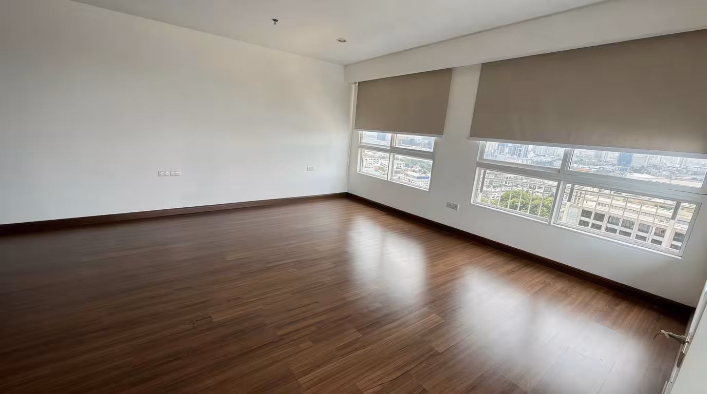 Empty modern apartment room with dark wood floors, white walls, and large city-view windows with roller blinds.