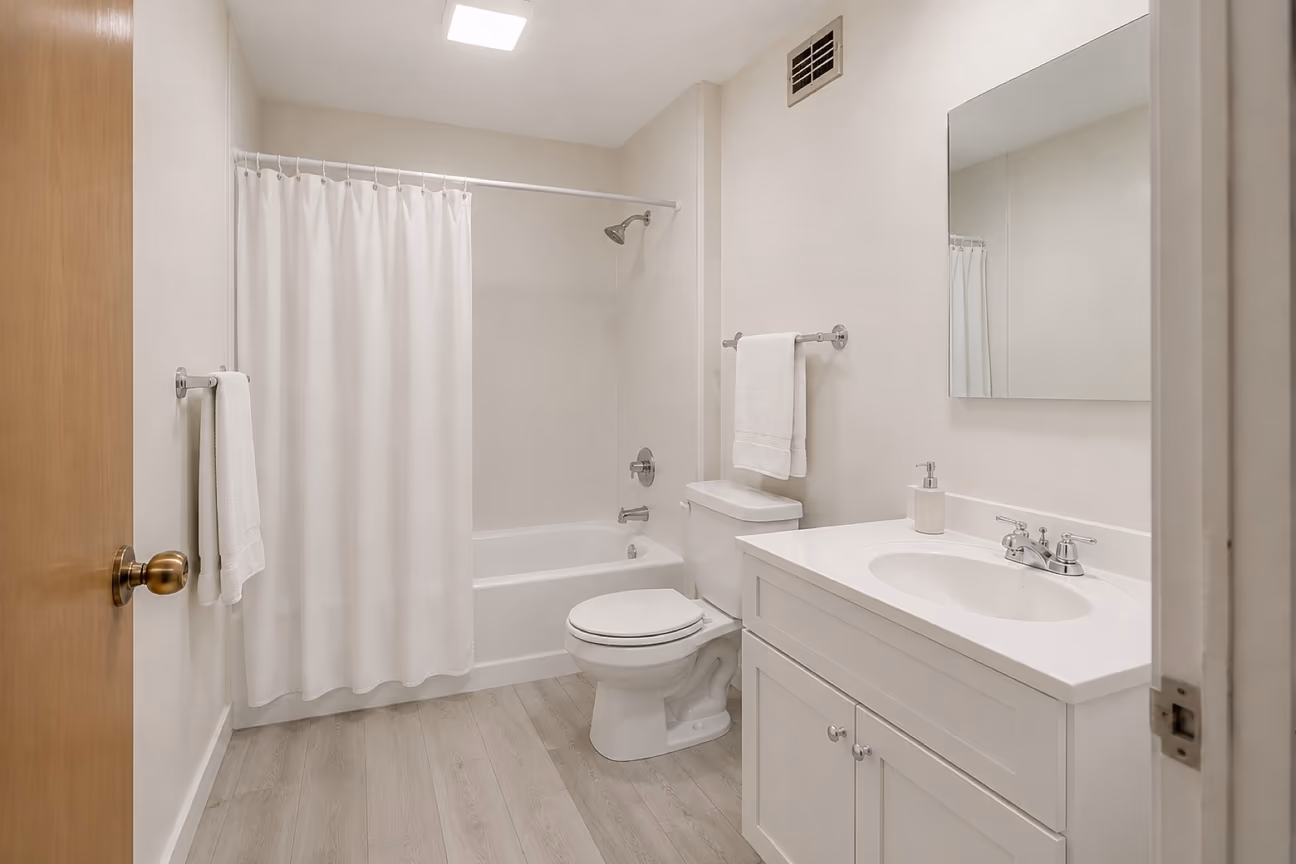 The same dated bathroom after a cosmetic refresh, with painted walls, a white fabric shower curtain, grey vinyl plank flooring and a white shaker vanity