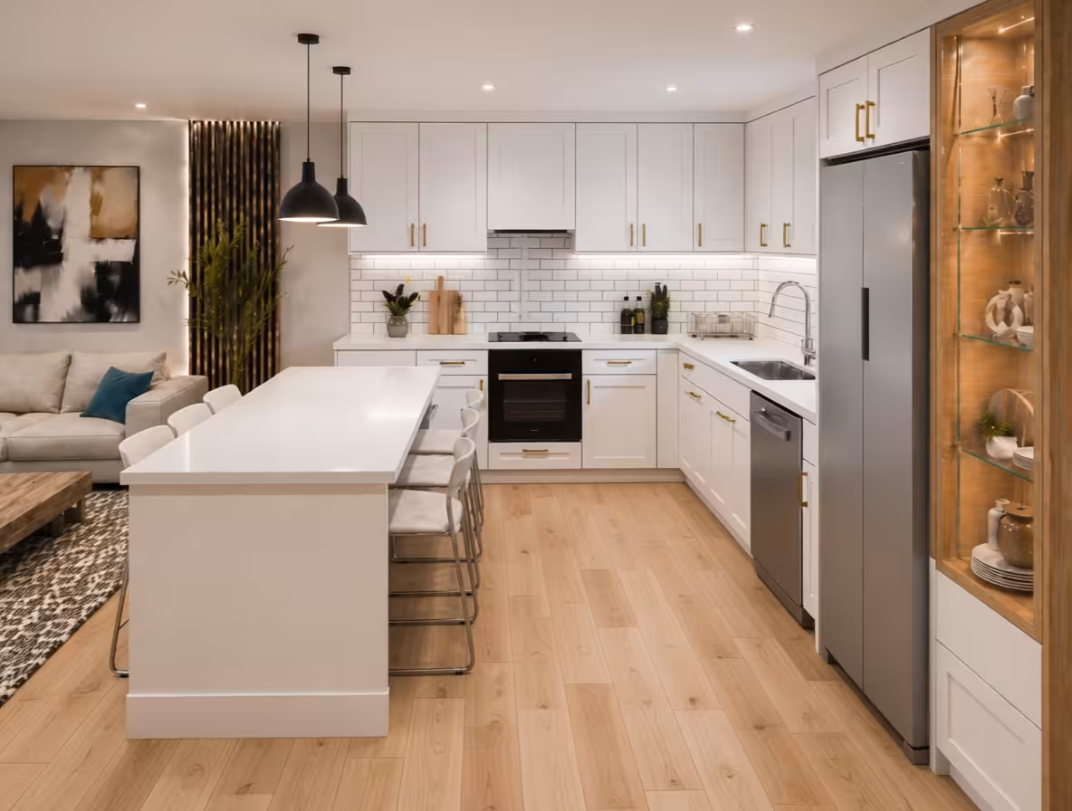 Modern open-concept kitchen with white cabinetry, large island seating, black pendant lights, brass hardware, and pale wood flooring