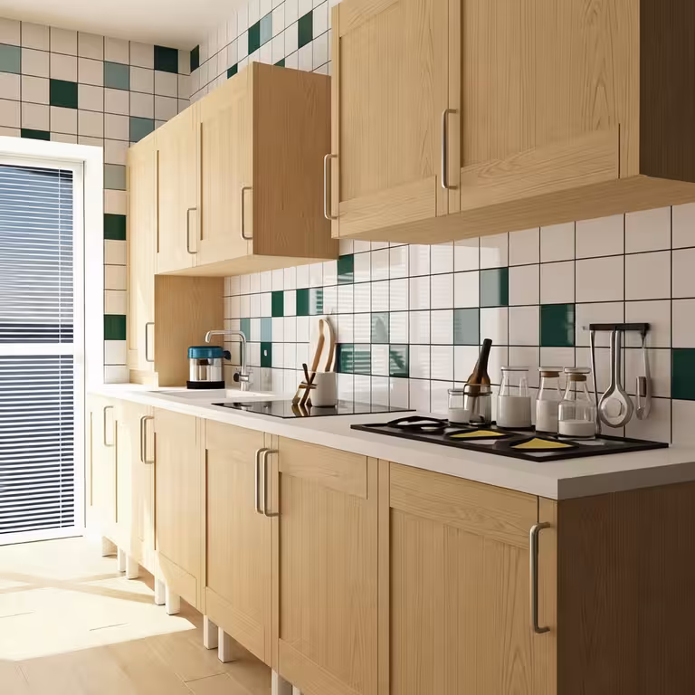 Modern single-wall kitchen with light wood cabinetry, white countertops, green and white tiled backsplash, sleek stovetop, and natural light.