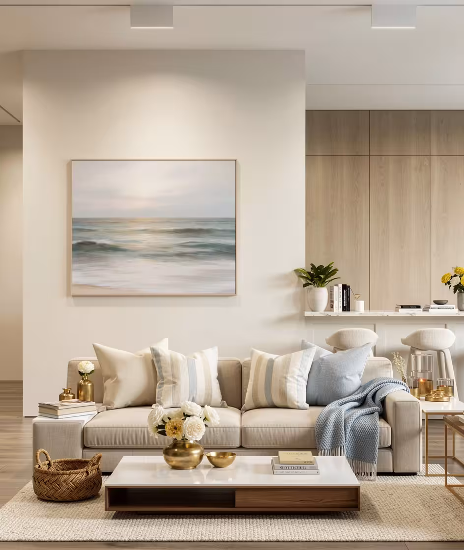 Contemporary living room with neutral beige sofa, striped and solid pillows, soft blue throw, ocean artwork, gold accents, woven basket, and light wood cabinetry.