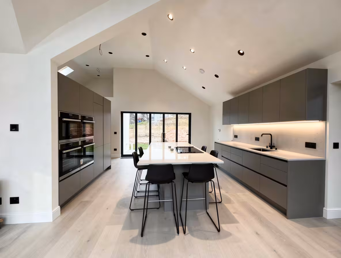 Contemporary galley kitchen with matte gray cabinets, waterfall island, vaulted ceiling, and minimalist modern design.