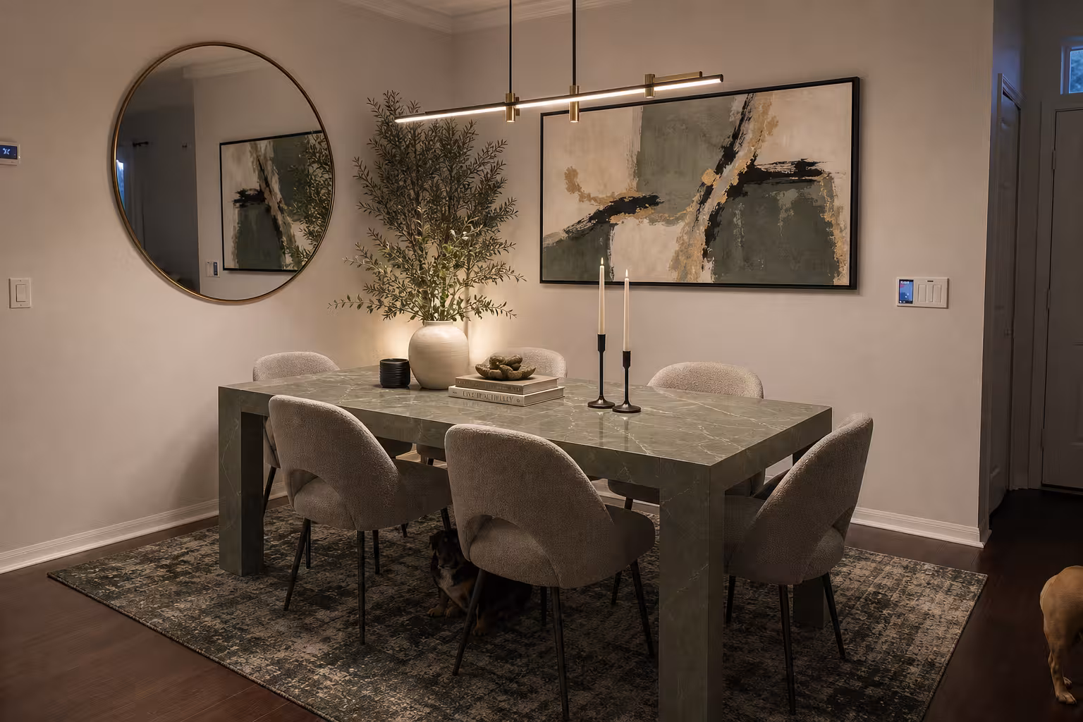 Modern dining room with sage green marble table, boucle dining chairs, abstract wall art, and brass linear lighting
