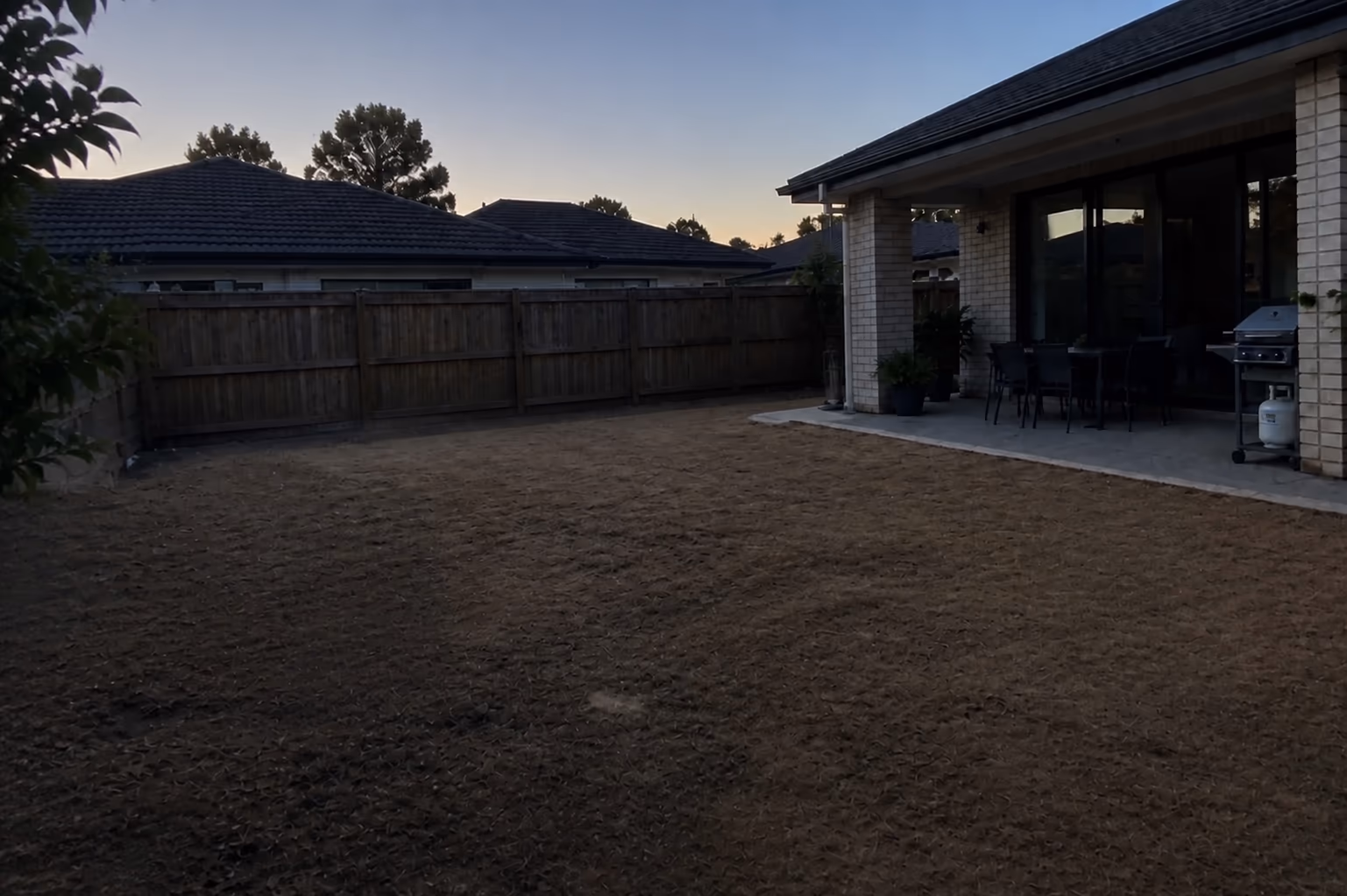 A dark photo of a backyard taken at dusk, with the lawn and fence barely visible