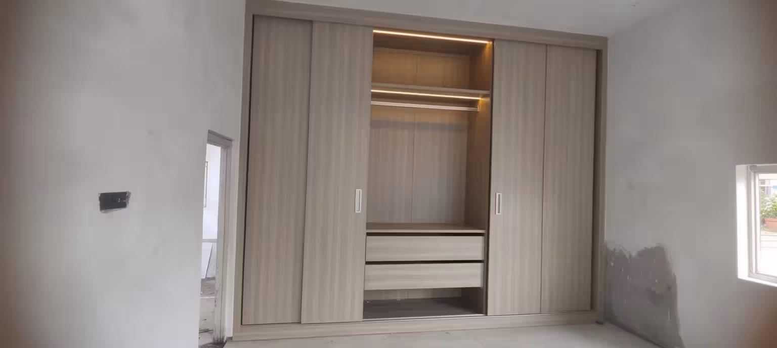 Modern built-in sliding wall wardrobe with light wood panels, integrated LED lighting, open shelves, and storage drawers.