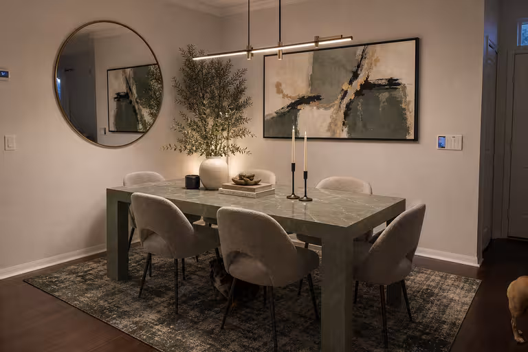 Modern dining room with sage green marble table, boucle dining chairs, abstract wall art, and brass linear lighting
