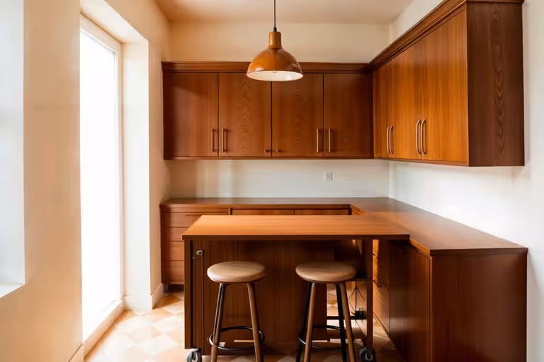 Mid-Century Modern kitchen with warm wood cabinetry, minimalist pendant light, two wooden stools, and soft natural light.
