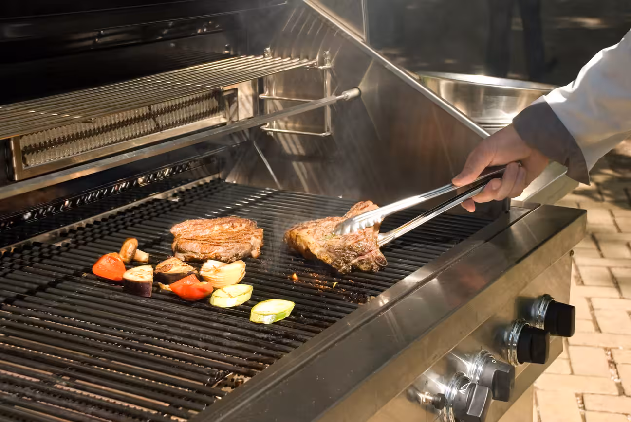 Grill and griddle station for restaurants in an outdoor kitchen setting with chef preparing barbecue on flat-top and grill
