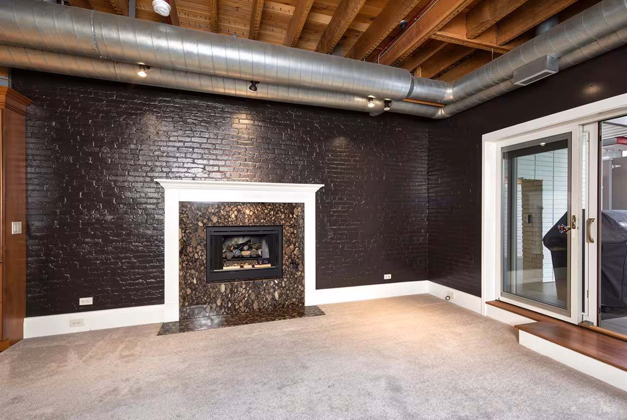 Industrial loft living room with exposed wood beams, black brick fireplace wall, metal ductwork, and modern open interior.