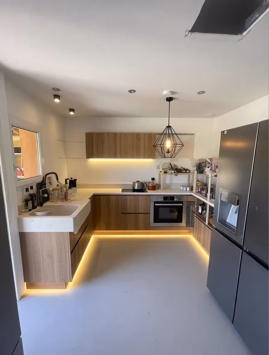A contemporary u-shaped kitchen with wood cabinets, white countertops, under-cabinet and floor LED lighting, stainless steel appliances, minimalist pendant light.