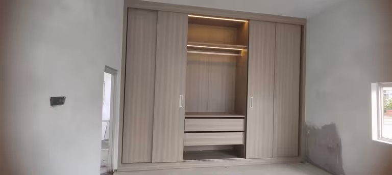 Modern built-in sliding wall wardrobe with light wood panels, integrated LED lighting, open shelves, and storage drawers.