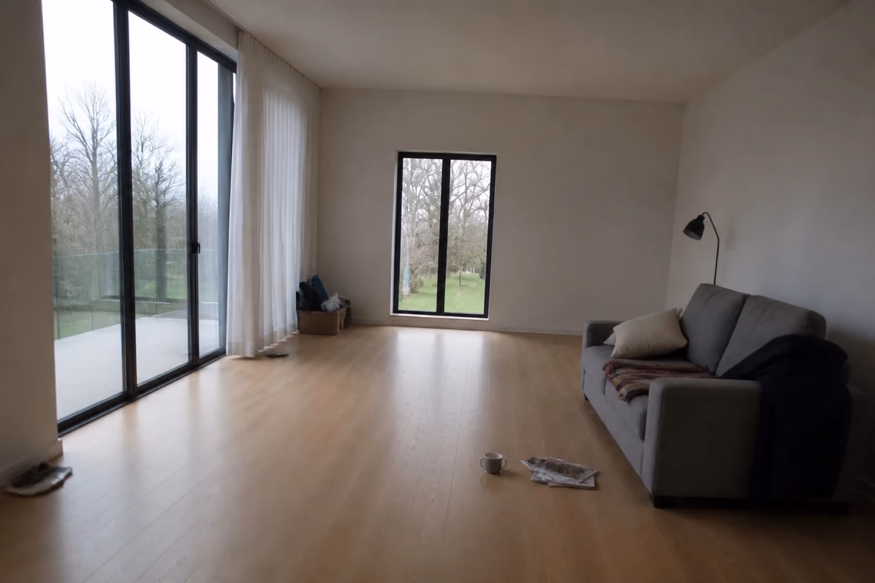 A dim cluttered photo of the same room with a coat over the sofa and litter on the floor