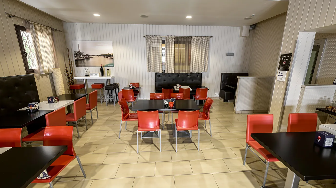 Dining area featuring black tables, bright red chairs, beige tiled floor, white paneled walls, and black leather bench seating.