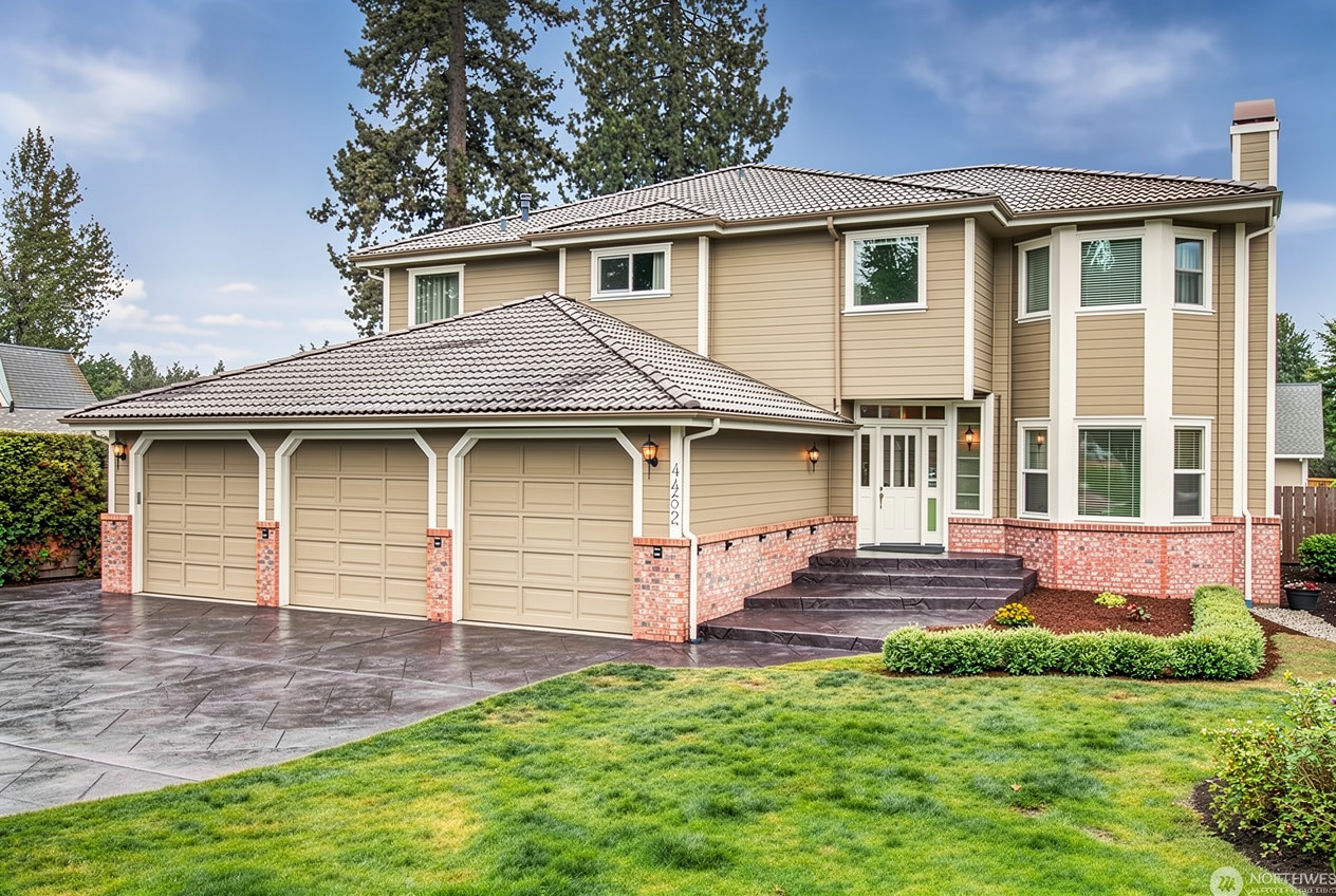 Two story suburban house with beige siding, brick accents, attached garage, and concrete driveway