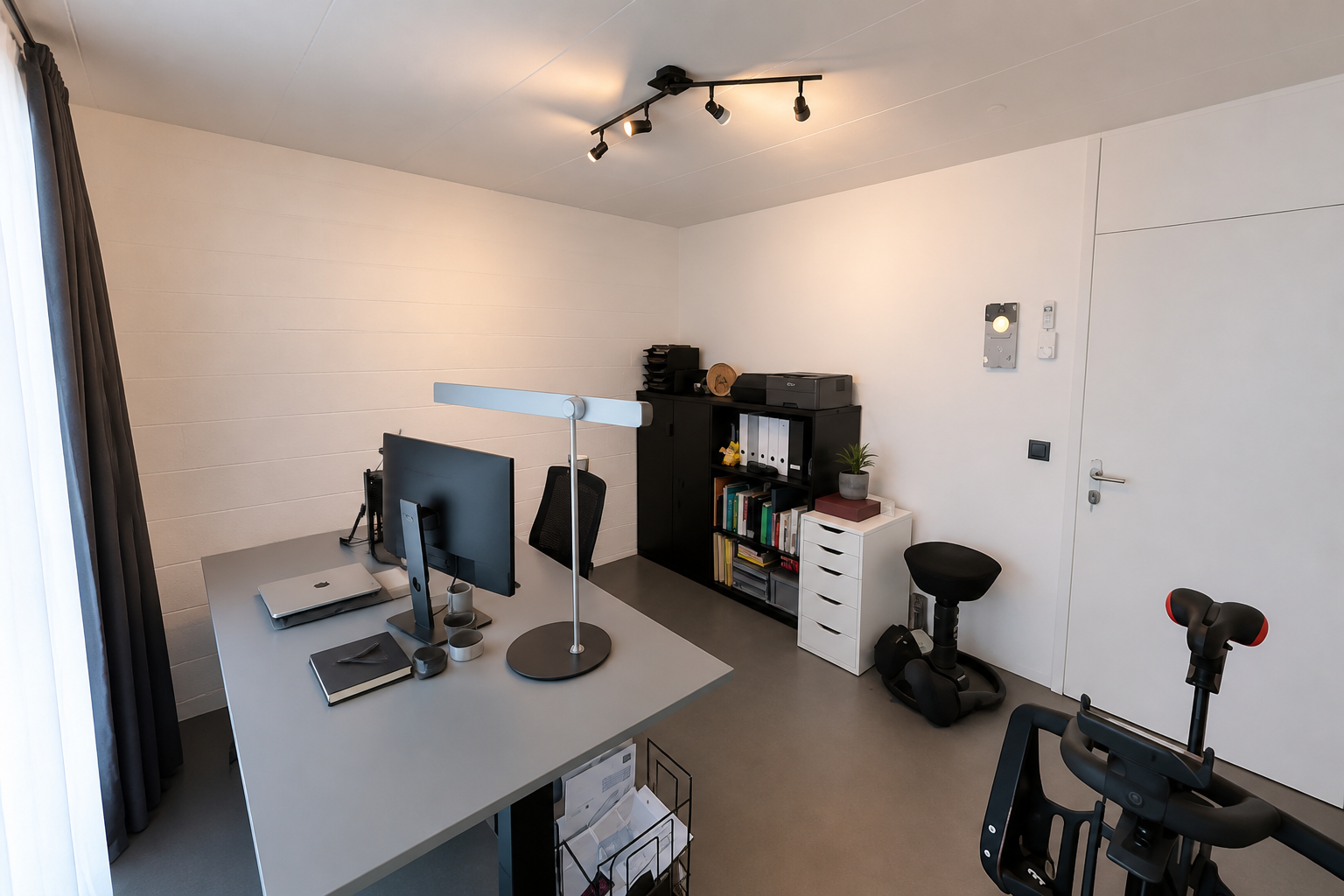 Minimal home office with desk setup, black shelving, and plain white walls