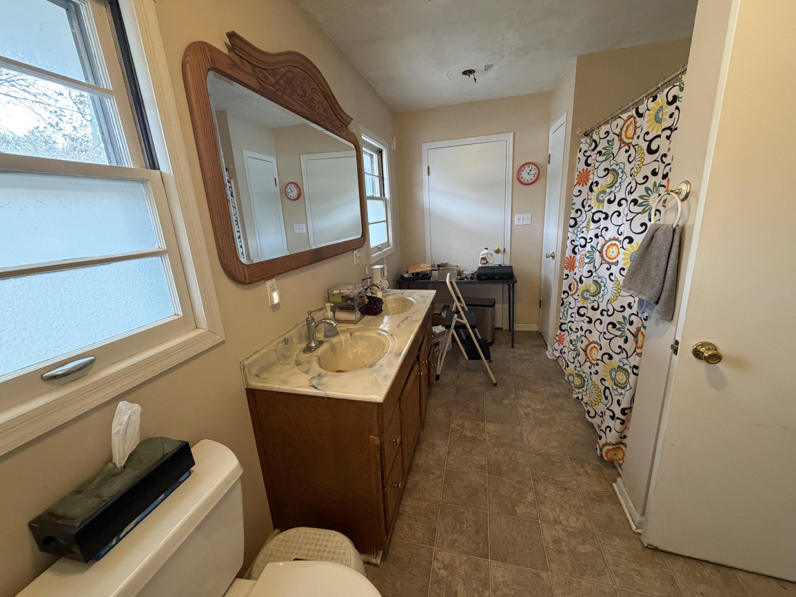 Bathroom with dark wood vanity, patterned shower curtain, beige walls, and framed wood mirror