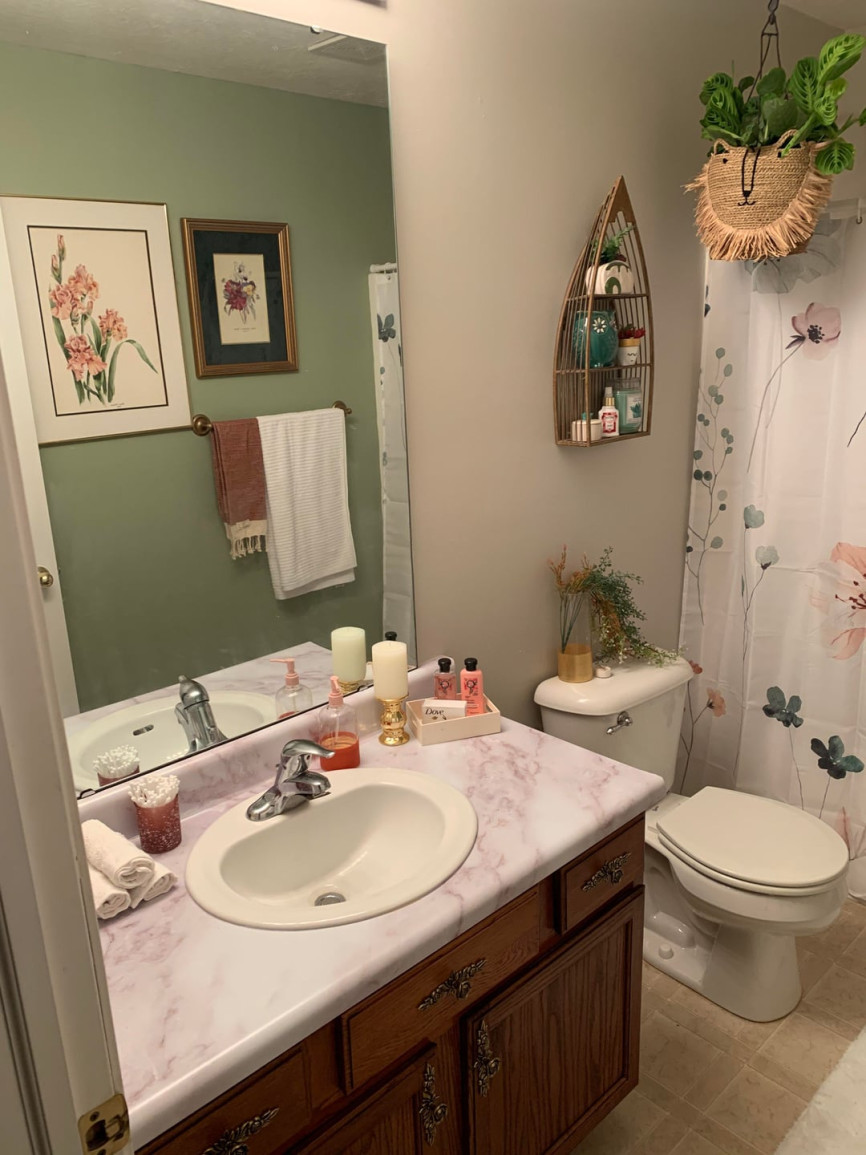 Small bathroom with pink marble countertop, floral shower curtain, green wall paneling, and decorative accessories