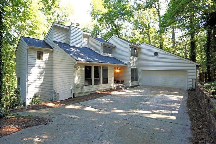 Two story suburban house with light gray siding, attached garage, concrete driveway, and wooded surroundings