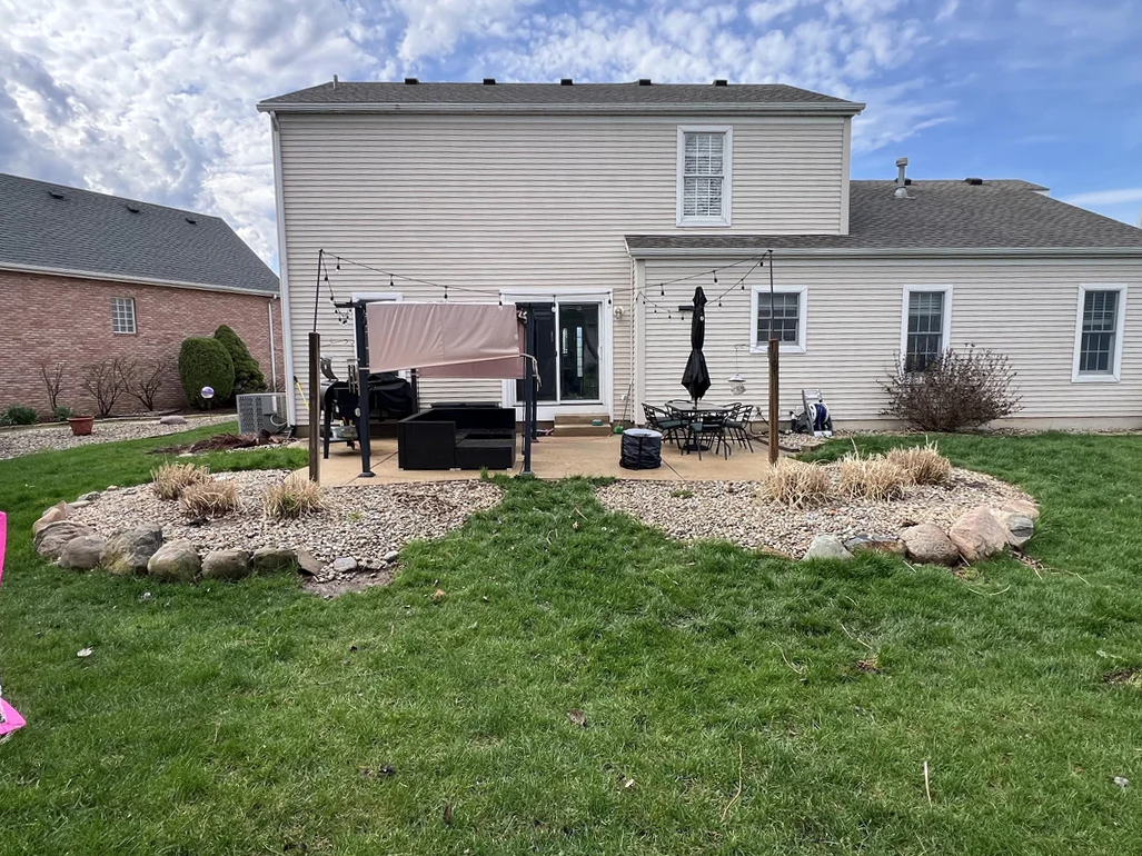 Backyard with simple patio seating, sparse rock beds, and open grass lawn