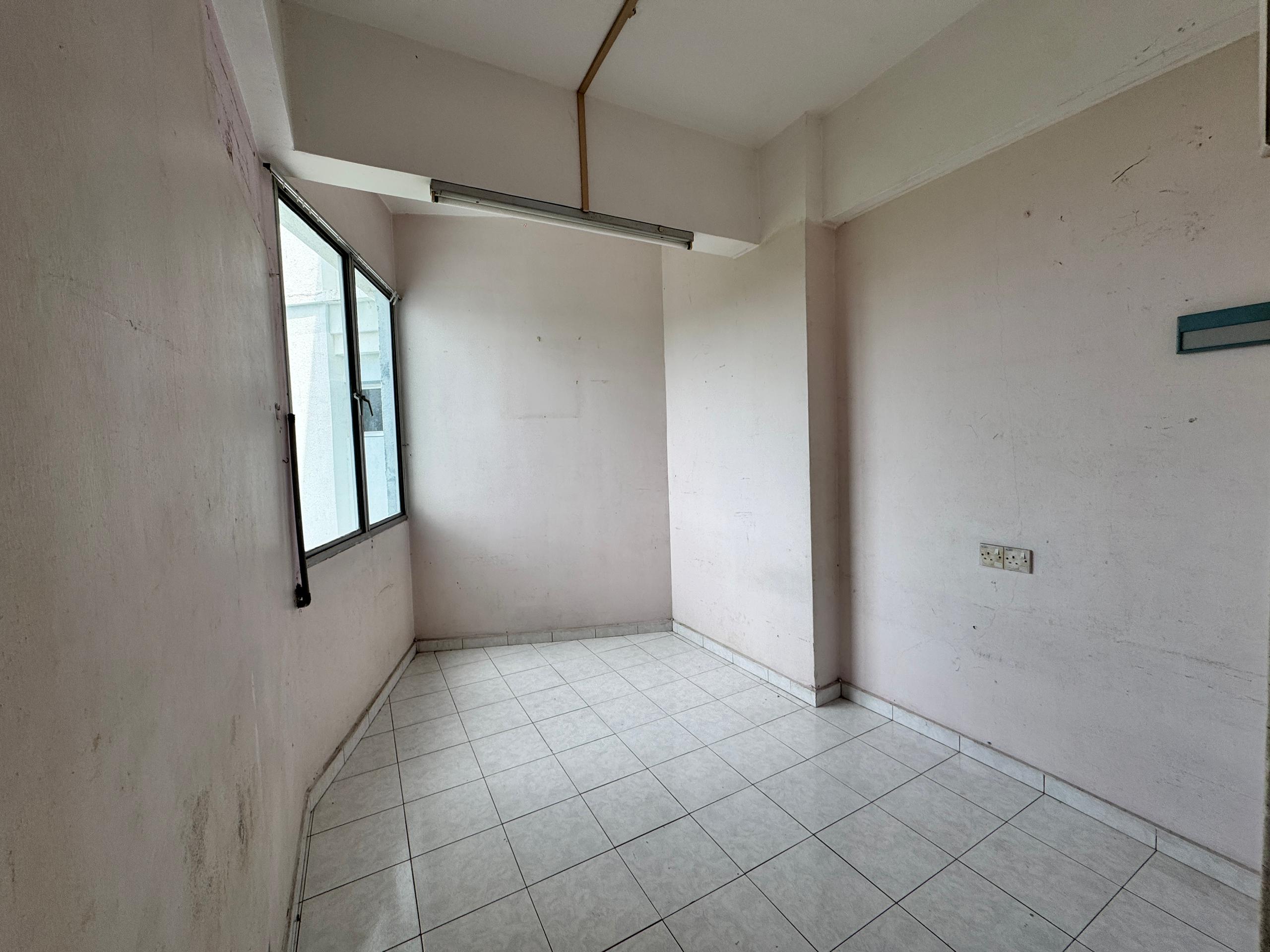 Empty, narrow room with plain off-white walls, tiled floor, a single window, exposed fluorescent light fixture.