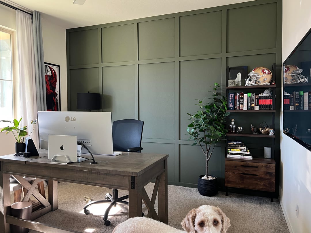Home office with dark green paneled wall, wooden desk, and open shelving