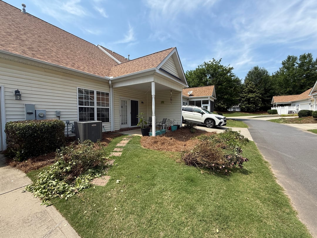Front yard with sparse landscaping, overgrown shrubs, and uneven mulch beds