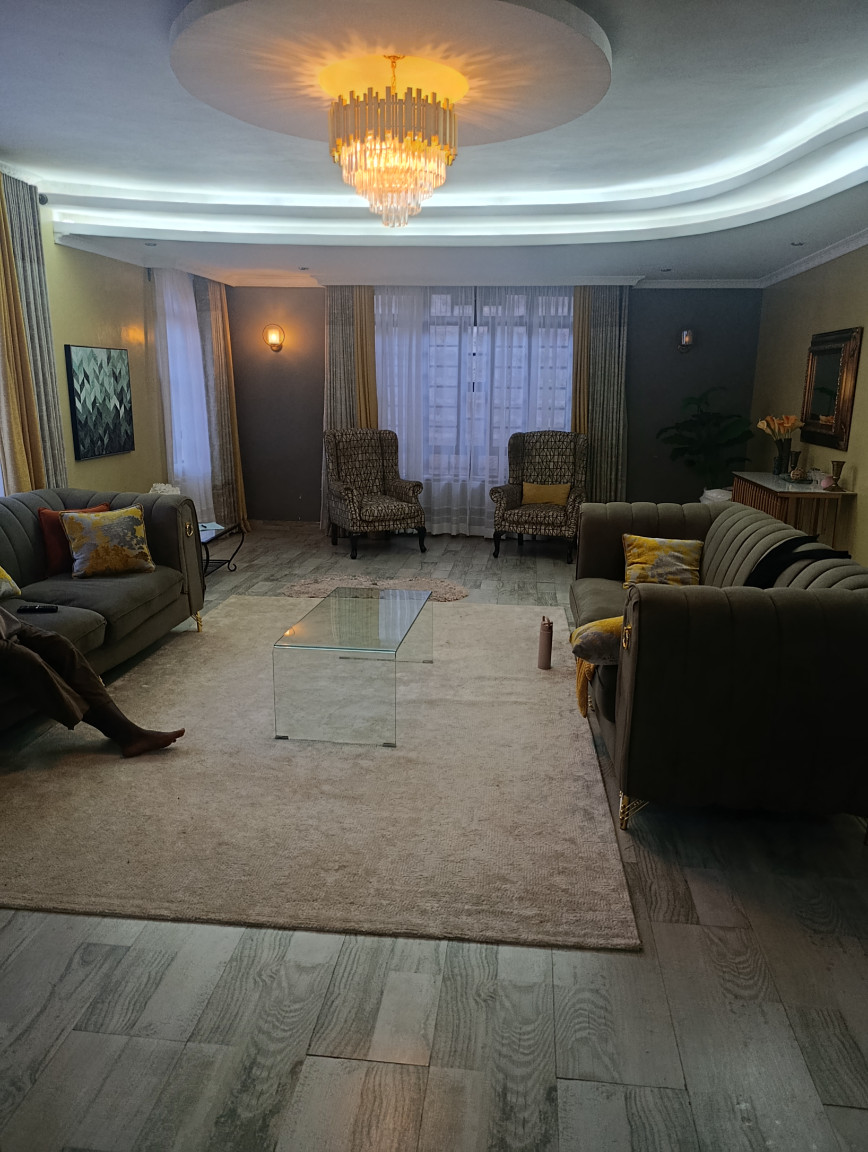 Traditional living room with dark sofas, patterned armchairs, carpet flooring, and curtained windows