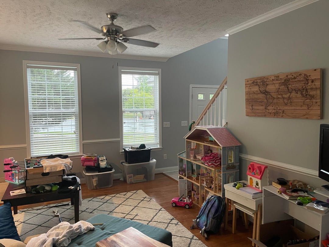 Family living room play area with dollhouse, kids desk, storage bins, gray walls, and hardwood flooring