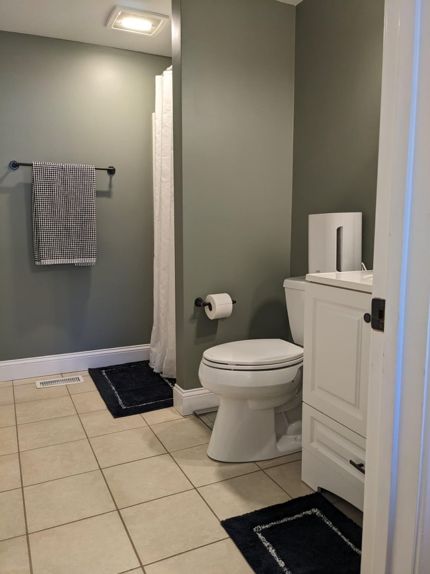 Small bathroom with green walls, white vanity, toilet, shower curtain, and beige floor tiles