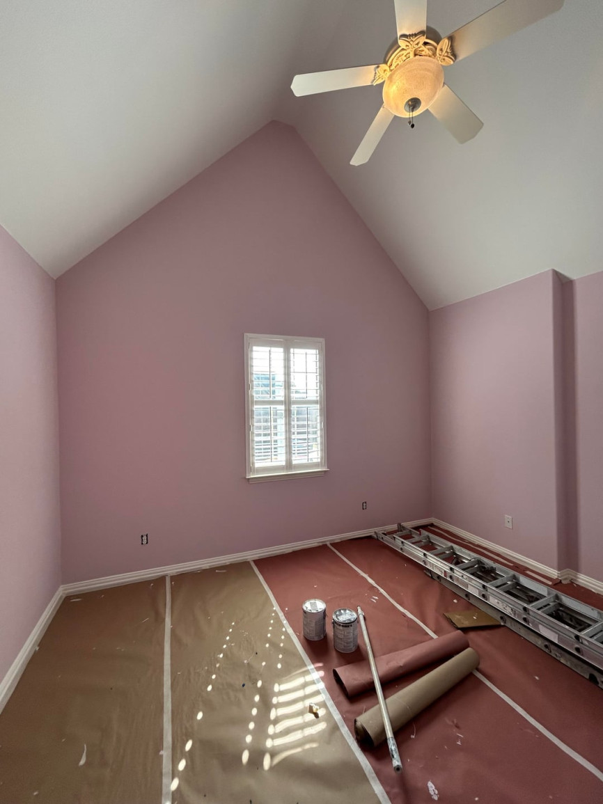 Empty room with blush pink walls, vaulted ceiling, unfinished flooring, and single centered window