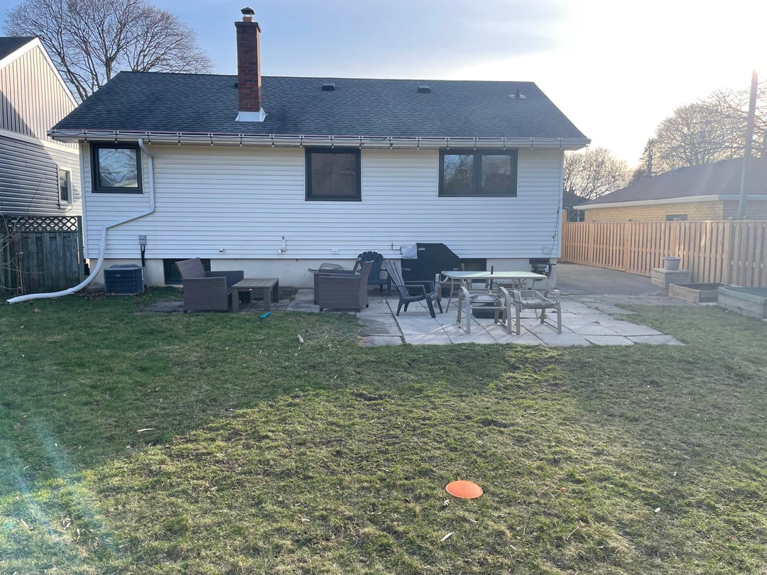 Suburban backyard with patio furniture, open lawn, white house siding, and wooden fence