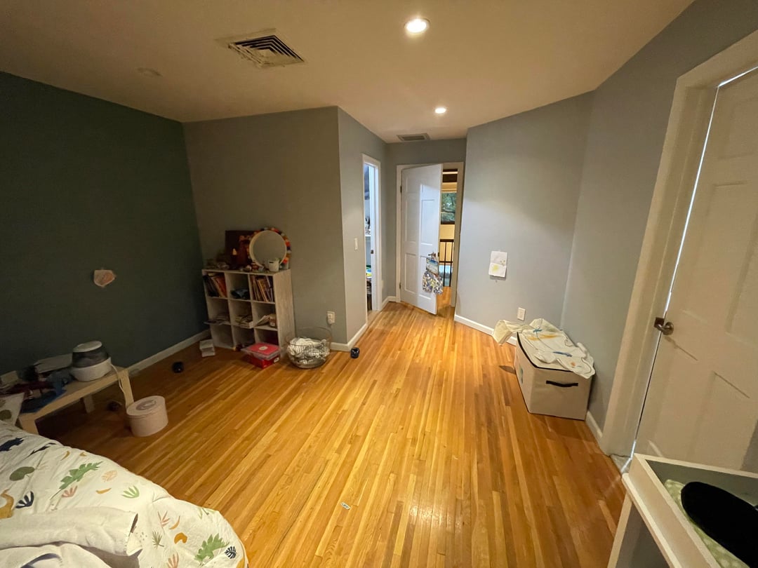 Kids bedroom with gray walls, hardwood flooring, scattered toys, and open floor space beside a dark accent wall.