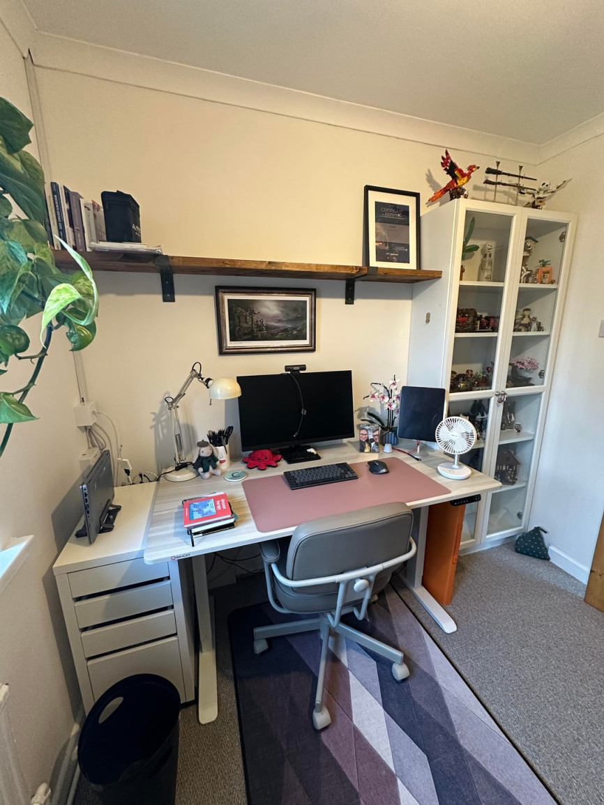Small home office with desk setup, floating shelf, and glass display cabinet