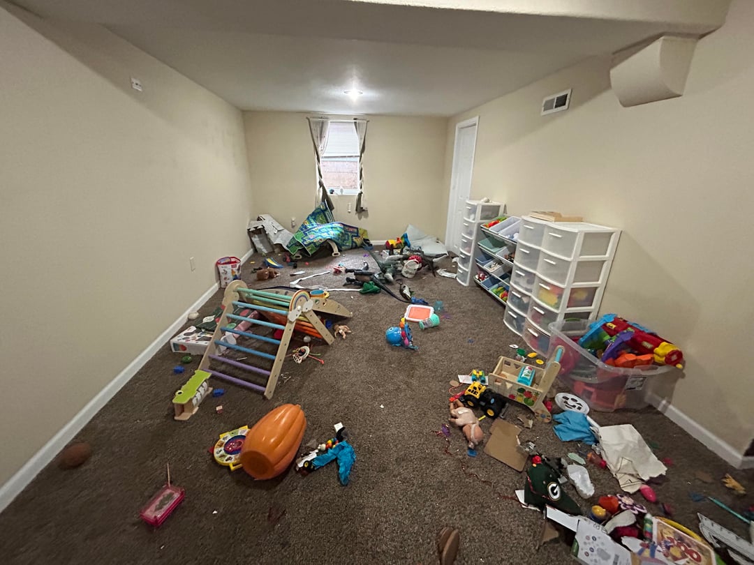 Basement kids playroom with scattered toys, plastic storage bins, carpet flooring, and open unfinished layout
