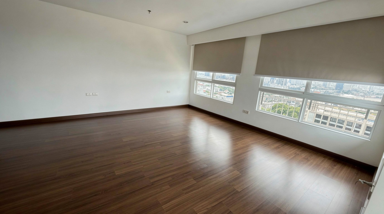 Empty room with smooth dark wood flooring, white walls, large windows with beige roller blinds, and bright natural light.