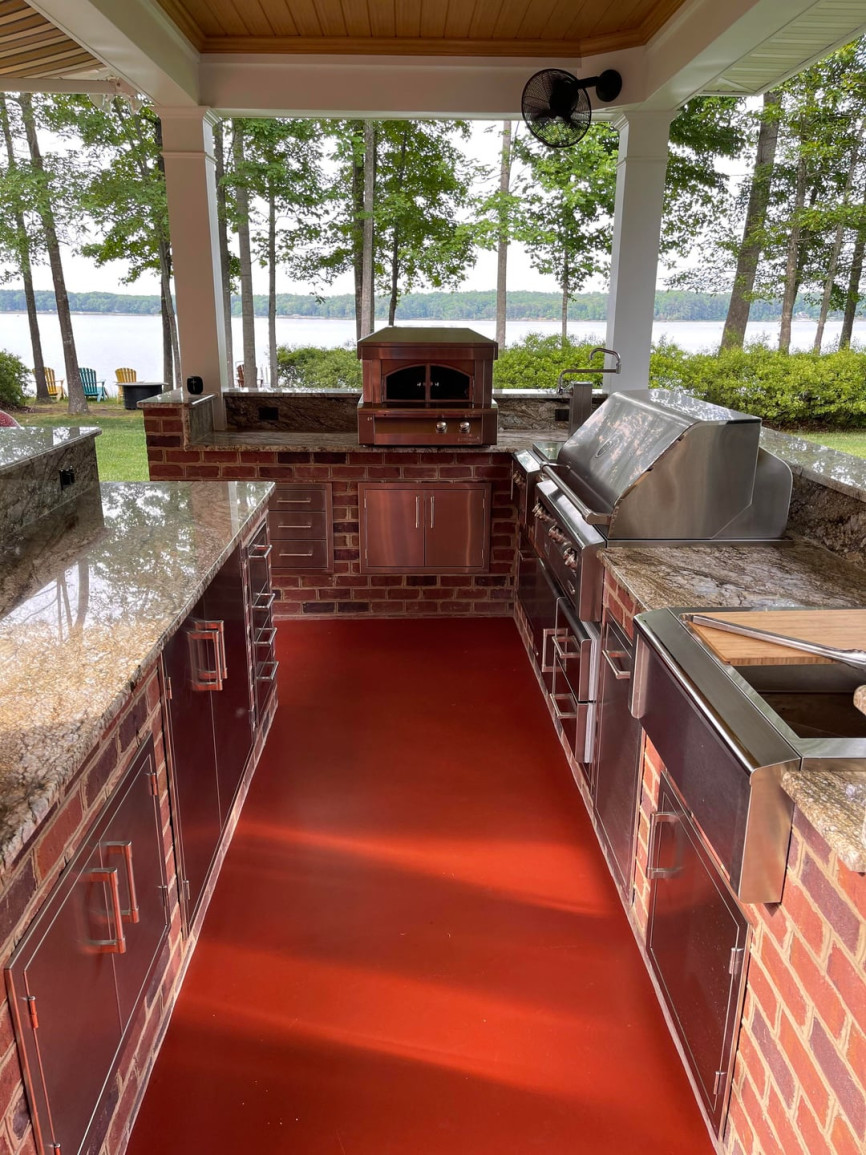 Outdoor kitchen with red brick base, granite countertops, stainless steel appliances, and lakefront view.