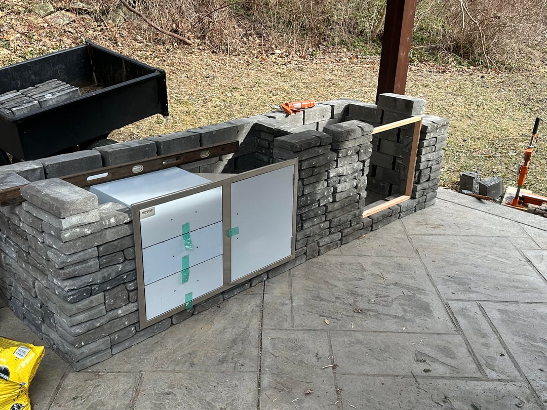 Partially built outdoor kitchen with unfinished stone structure and concrete patio