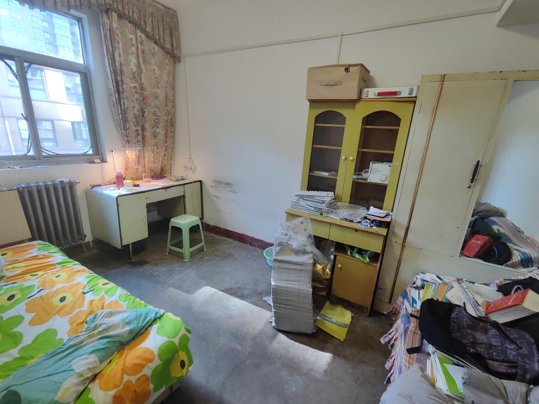 Kids bedroom with mismatched storage cabinet, cluttered desk area, floral bedding, and unfinished organization.