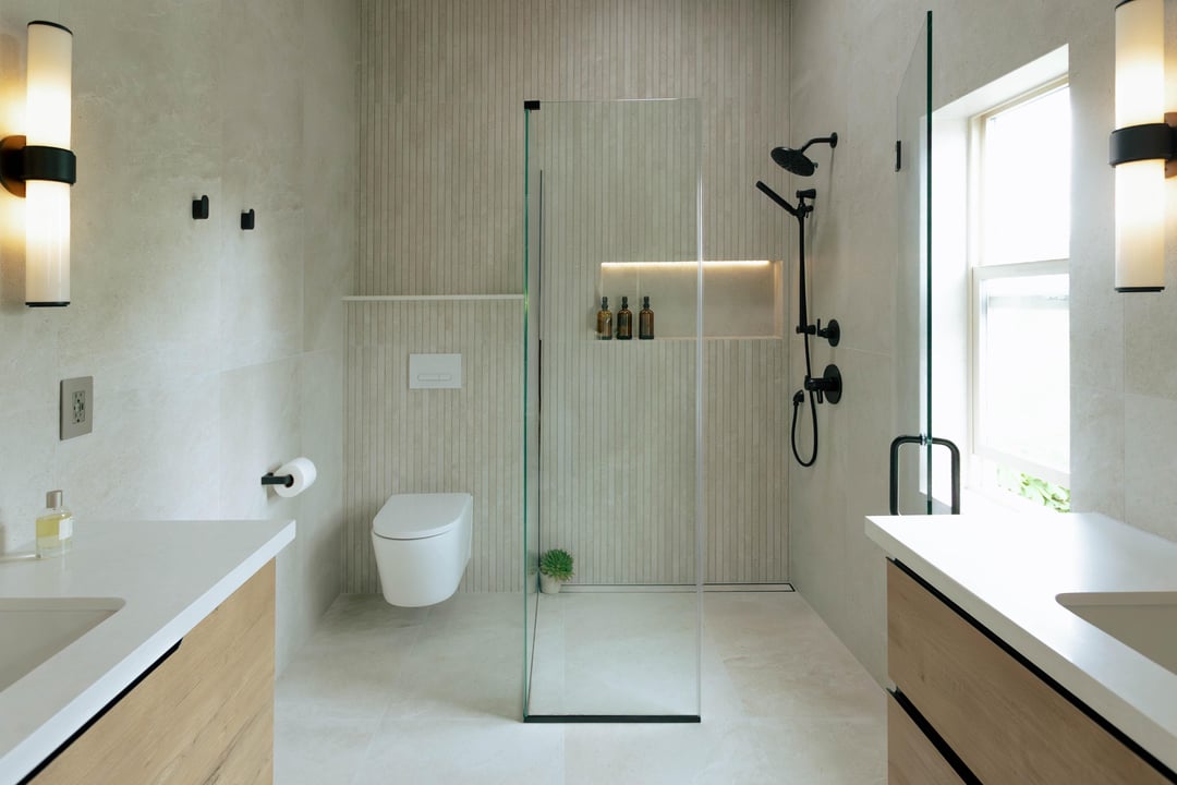Minimal bathroom with white walls, floating vanity, glass shower enclosure, toilet, and natural window lighting