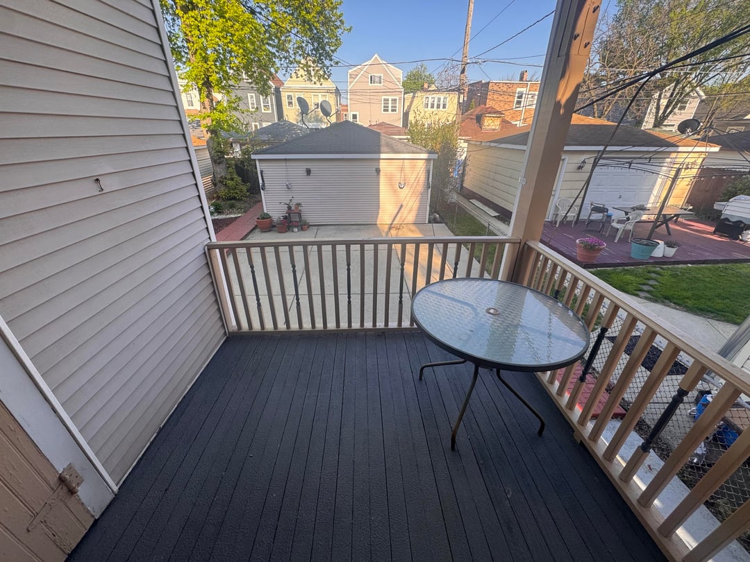 Empty apartment balcony with dark flooring, wood railing, and glass outdoor table