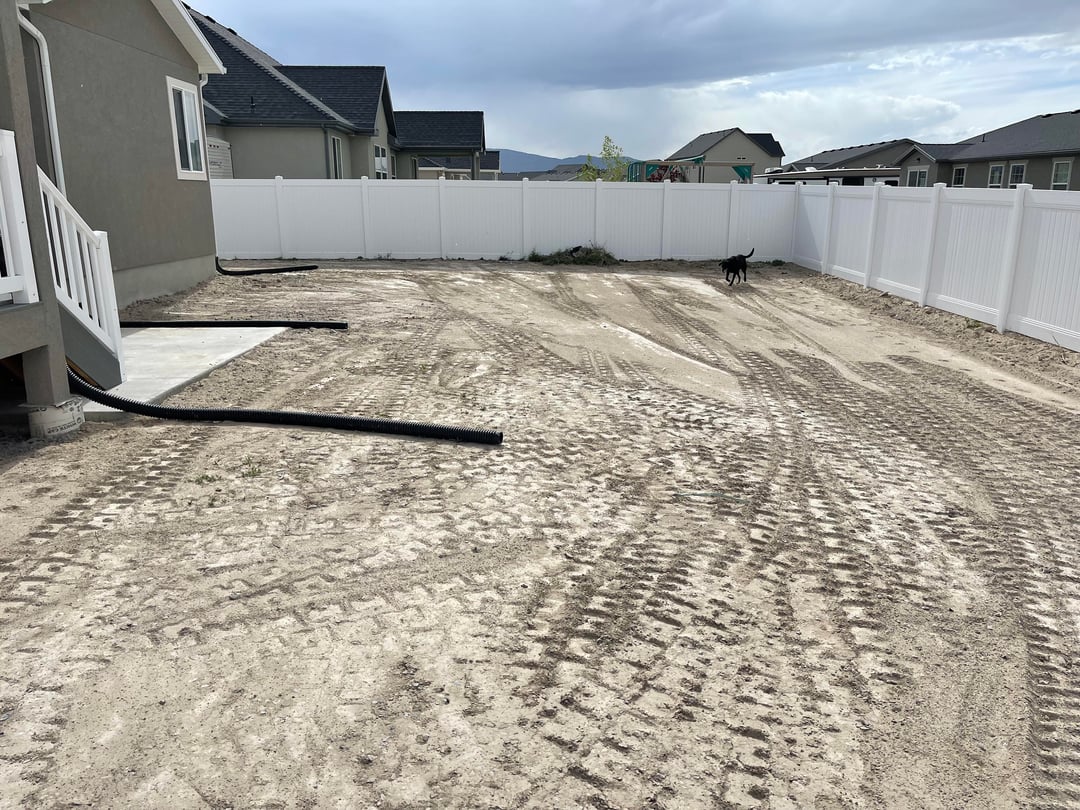 Bare dirt backyard with white vinyl fencing and unfinished grading