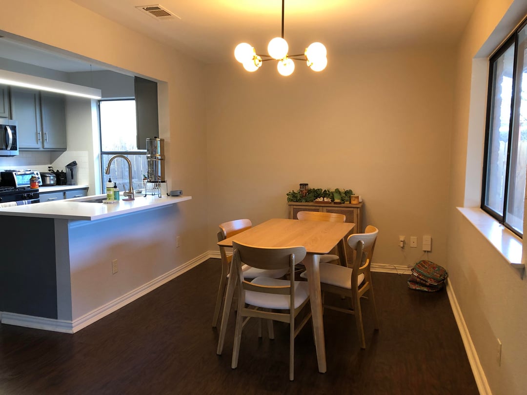 Dining area with wood table, modern chairs, beige walls, dark flooring, and simple pendant lighting