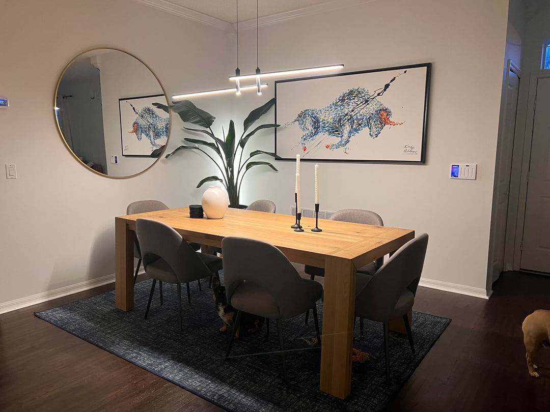 Dining room with wood dining table, gray upholstered chairs, round mirror, and animal artwork