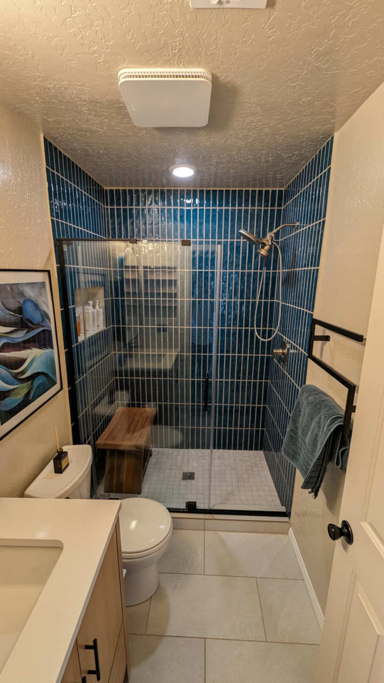 Bathroom with dark blue vertical tiles, glass shower enclosure, wood bench, and black towel bars