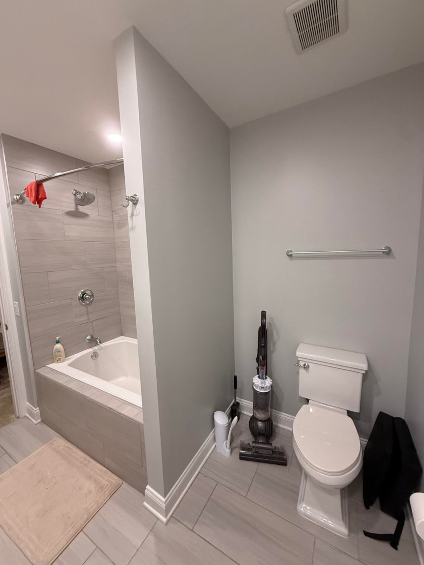 Bathroom with gray walls, bathtub shower combo, white toilet, and chrome shower curtain rod