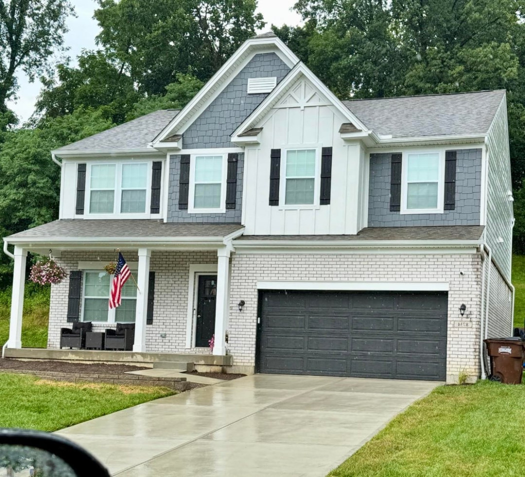 Two story suburban house with white brick exterior, black garage door, front porch, and farmhouse detailing